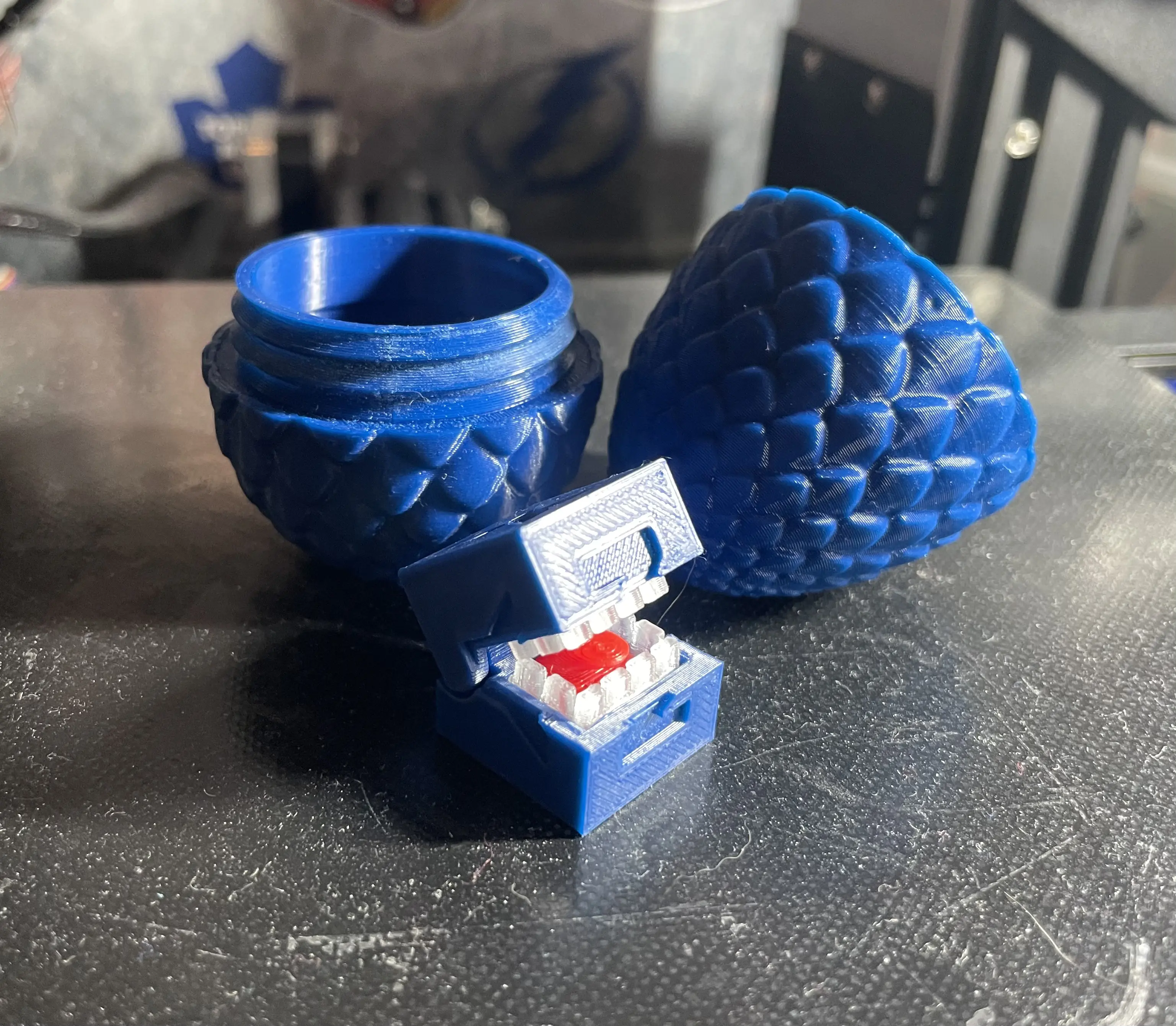 A blue, 3D printed, dragon egg with threaded edges to screw together and a blue, 3D printed calibration cube for a 3D printer that has teeth and a tongue
