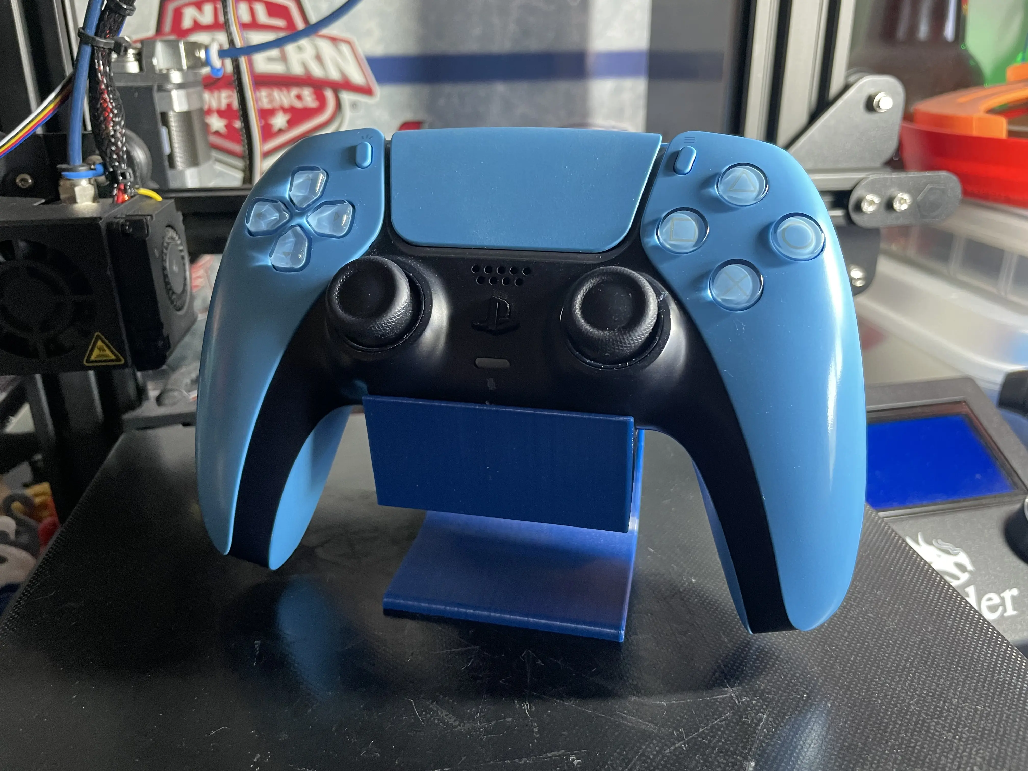 A blue, 3D printed stand for a Playstation 5 controller with a controller on it